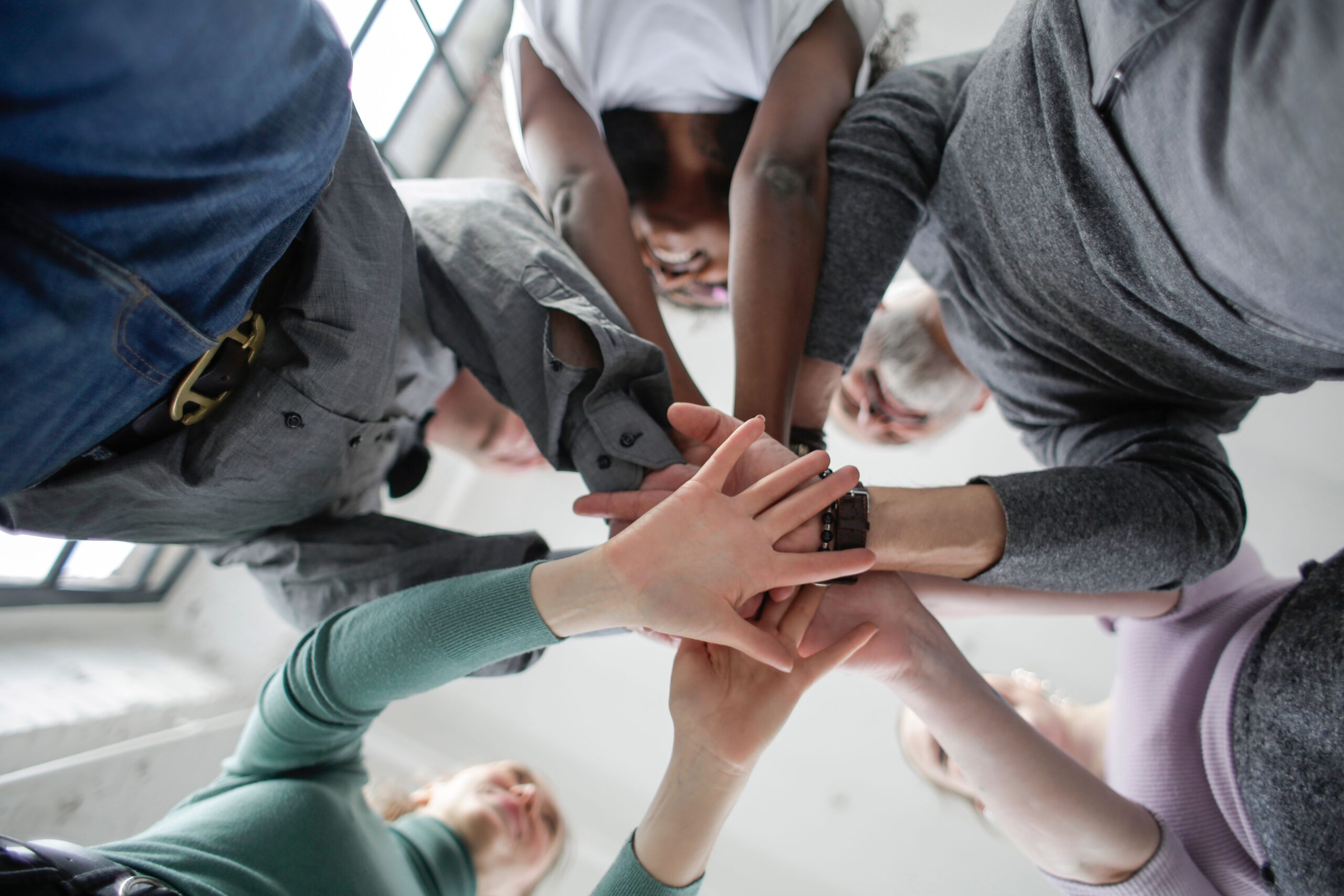 Low angle view of a diverse group uniting hands indoors, symbolizing teamwork and collaboration.